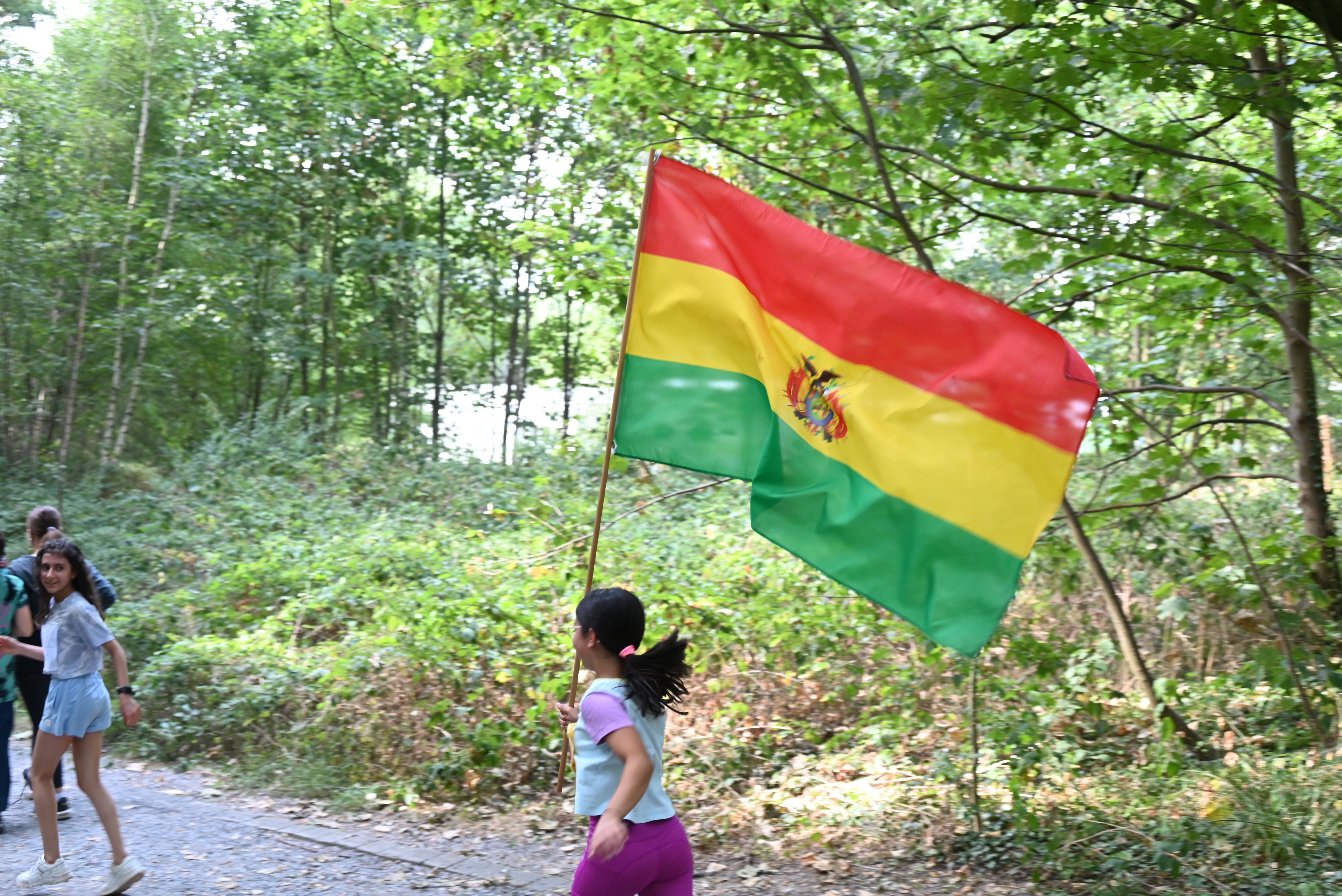 Es ist die Rückseite eines sportlich gekleideten Mädchens beim Spendenlauf zu sehen, welche die bolivianische Flagge trägt. 